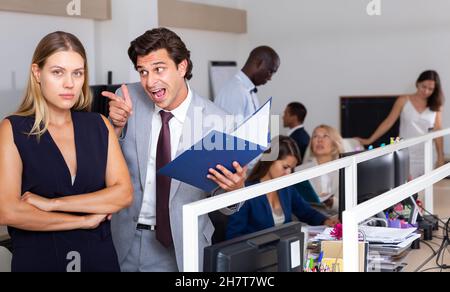 Capo arrabbiato maschio che accusava una giovane donna che lavorava in ufficio Foto Stock