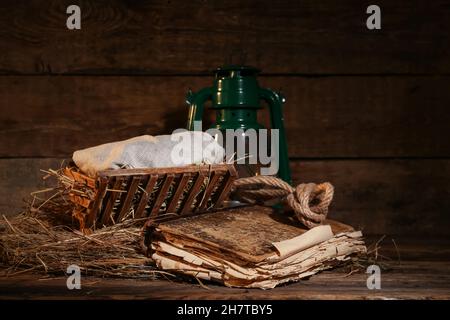 Mangiatoia con bambino, vecchio libro e lanterna su sfondo ligneo. Concetto di storia di Natale Foto Stock