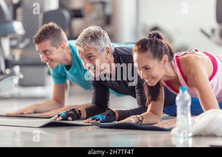 Gruppo di persone in varie età e sesso divertirsi mentre si fa esercizio di gruppo di gomito in palestra. Foto Stock