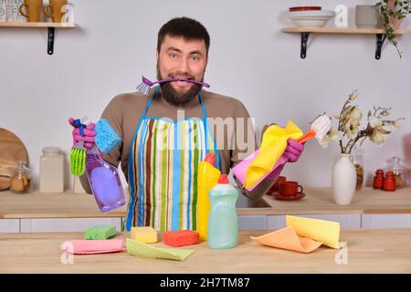 Confuso giovane bel bearded uomo in cucina, non hanno idea di cosa fare con tutti i suoi detergenti, spazzole, spray Foto Stock
