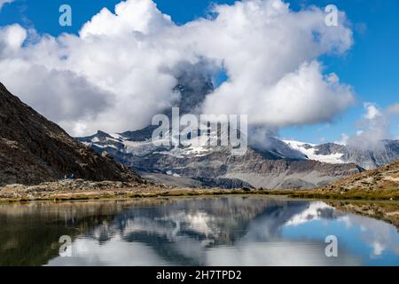 Vista panoramica sull'acqua del Riffelsee vicino Zermatt, Svizzera verso il Cervino parzialmente coperto da nuvole bianche, anch'essa riflessa nella Foto Stock