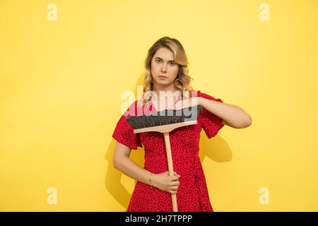 Donna con capelli biondi lunghi, abito rosso fissa con intanto la macchina fotografica, piangendo per aiuto. Pulizia locali di casa. Stanco. Sfida negli occhi. Studio girato su Foto Stock