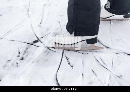 Foto ravvicinata dei pattini. Pattini di pattinaggio a figura bianca indossati sui piedi della persona, attingendo sul ghiaccio dalle lame dei pattini Foto Stock