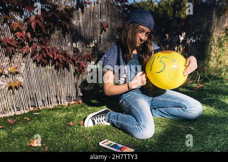 Ragazza attivista adolescente che dipinge un palloncino giallo in giardino in una giornata di primavera. Disegno di una chiamata per impedire che la temperatura della terra aumenti vicino Foto Stock