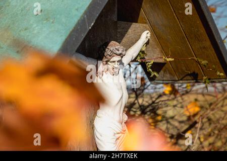 Una croce lungo la strada in Baviera, foglie d'autunno marroni incorniciano Gesù Foto Stock