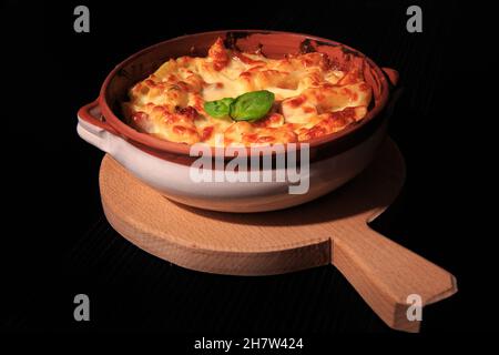 Penne pasta in un piatto rustico su un piatto di legno isolato su sfondo nero. Foto Stock