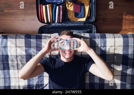 Ritratto divertente di uomo giovane felice durante la valigia di imballaggio e pianificare l'avventura di viaggio. Foto Stock