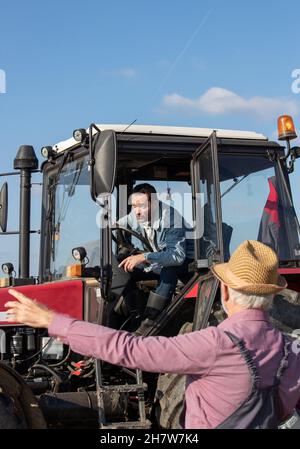 Agricoltore maturo che guida il trattore e parla con un uomo anziano sul campo Foto Stock