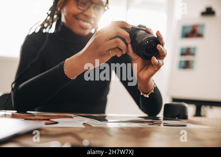 Fotografo che tiene una fotocamera reflex digitale nella sua fotocamera nel suo ufficio domestico. Giovane donna creativa sorridente allegro mentre lavora alla sua scrivania. Freelan femminile Foto Stock