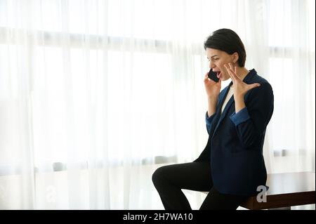 Donna d'affari, dipendente femminile, giovane imprenditore sudore, sostiene, gesti con le mani mentre parla al telefono, seduto al bordo di un tavolo Foto Stock