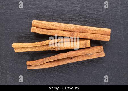 Tre bastoni di cannella fragrante su una pietra ardesia, primo piano, vista dall'alto. Foto Stock