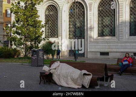 Un senzatetto nel sacco a pelo si trova addormentato su una panchina di fronte ad una chiesa di Bologna, Italia. Foto Stock