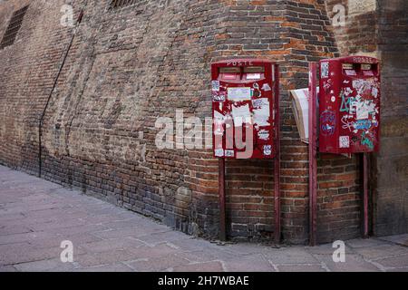 Su un muro di Bologna, in Italia, ci sono due caselle rosse cosparse di graffiti. Una scatola di pizza vuota è stata messa dietro uno di loro. Foto Stock