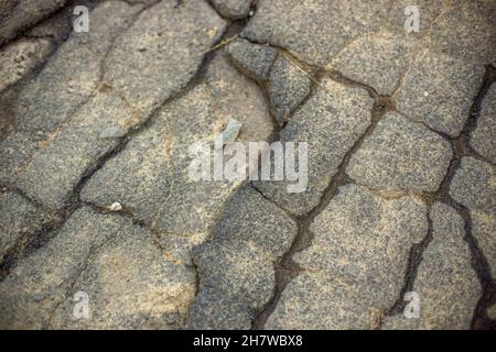 Primo piano di una strada asfaltata rotta in crepe bagnate. Foto Stock