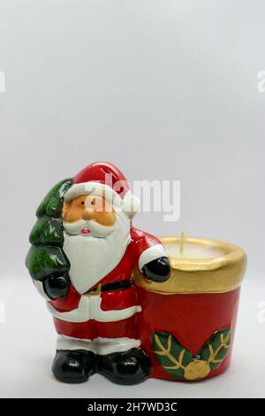 Babbo Natale con corpo rosso, albero di Natale verde e candela, personaggio in ceramica di Babbo Natale su sfondo bianco, decorazione natalizia, biglietto di Capodanno Foto Stock