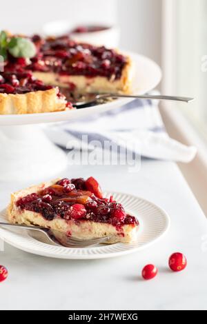 Una fetta di crostata di cheesecake al mirtillo con l'intera torta dentro dietro. Foto Stock