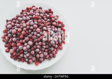 Mirtilli rossi freschi congelati in gelo in ciotola di ceramica bianca, foto in primo piano orizzontale su sfondo bianco Foto Stock