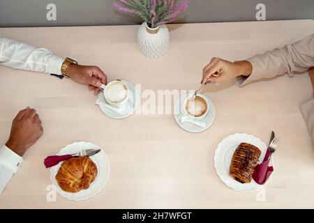 Colazione. Uomo e donna che fanno colazione in caffetteria. Caffè e panini. Pasticceria su tavola di legno. Prima colazione dei lavoratori. In caffetteria. Foto Stock