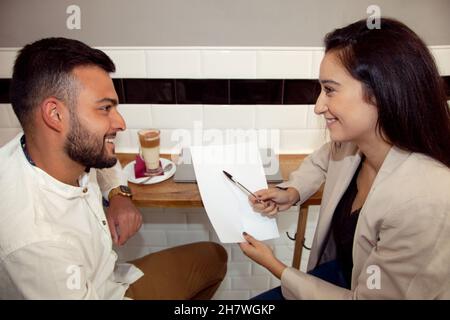 Coppia che controlla il loro lavoro. Coppia guardandosi l'un l'altro. Uomo e donna che rivedono i foglios. Ragazzo guardando la ragazza. Ragazza sorridente al ragazzo. Meeting di lavoro. Foto Stock