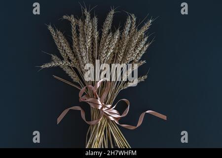 Un bouquet di spighe di grano legato con un nastro satinato su sfondo scuro. Foto orizzontale. Foto Stock