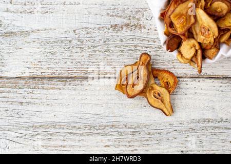 Un mucchio di fette secche di pere in sacchetto bianco su sfondo di legno. Patatine di frutta secca. Cibo vegano sano Foto Stock