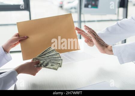 vista ritagliata del medico che mostra stop gesture al paziente con busta e dollari, anti-corruzione concetto Foto Stock