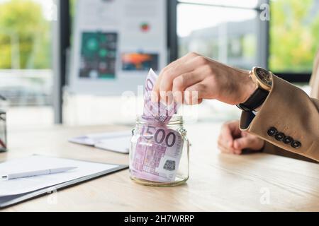 visione ritagliata dell'uomo d'affari che mette le banconote in euro in vaso di vetro, concetto anti-corruzione Foto Stock