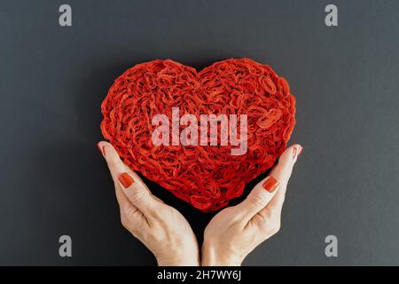 Cuore rosso in carta zaffinata su sfondo scuro nelle mani di una giovane donna. Il concetto di amore, dono, cura, Complimenti. Foto orizzontale. Foto Stock
