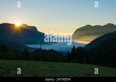 Nuvole basse come l'alba si infrange sulla Valle del Sauris vicino al villaggio alpino di Sauris di sopra, provincia di Udine, Friuli-Venezia Giulia, nord-est Italia. In ritardo Foto Stock