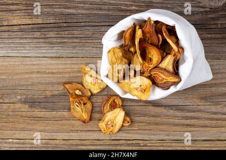 Un mucchio di fette secche di pere in sacchetto bianco su sfondo di legno. Patatine di frutta secca. Cibo vegano sano Foto Stock