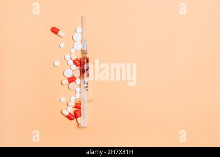 Pillole e compresse colorate con siringa su sfondo beige con spazio per la copia Foto Stock