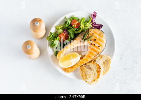 Bistecca di pesce di salmone alla griglia con lattuga e pomodori su un piatto di ceramica bianca Foto Stock