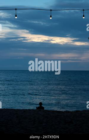un uomo seduto sulla spiaggia, al mattino Foto Stock