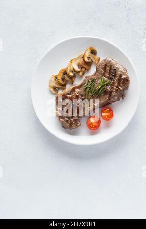 Bistecca di manzo alla griglia con funghi e spezie su un piatto di ceramica bianca. Vista dall'alto, spazio di copia Foto Stock