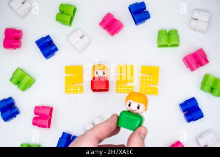 Blocchi di costruzione vintage colorati, giocattoli figure in plastica: Ragazza in 2022 numeri, ragazzo in mano, sfondo bianco. Foto Stock