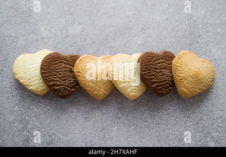 Biscotti multicolori a forma di cuore: Vaniglia, limone, cioccolato. Sfondo grigio, spazio di copia. Foto Stock