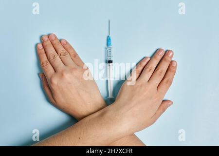 Antivaxer incrocia le mani vicino alla siringa con il vaccino Covid-19. Una persona che rifiuta l'immunizzazione contro il coronavirus. Concetto di scetticismo del Covid Foto Stock