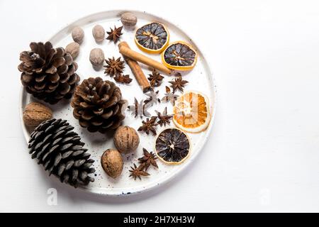 Composizione di Natale in una ciotola. Coni, noce moscata, cannella, fette di arancia secca, anice, Noci su un vassoio come decorazione domestica per il nuovo anno sul whi Foto Stock