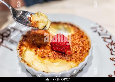 Macro primo piano di mano cucchiaio mangiare creme brulee piatto dessert con zucchero bruciato e fragola sulla crosta e segno fatto a mano in salsa di cioccolato per ha Foto Stock