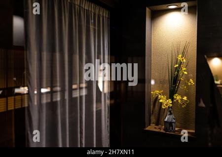 Tradizionale casa giapponese o hotel a casa ryokan con fiori gialli ikebana in decori in vaso illuminati da lampada in camera scura con tende a. Foto Stock