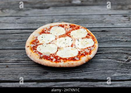 Piccola pizza fatta in casa closeup intero su tavola rustica in legno con provolone fuso e mozzarella e spolverate e salsa di pomodoro rosso come info italiano Foto Stock