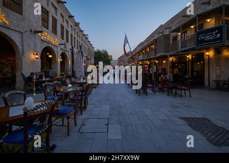 Souq Waqif Doha, Qatar luce naturale vista mostra la strada principale con caffè, ristoranti, persone a piedi e bandiera Qatar Foto Stock