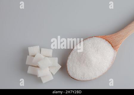 Zucchero granulato e cubetti di zucchero in cucchiaio di legno su sfondo bianco Foto Stock