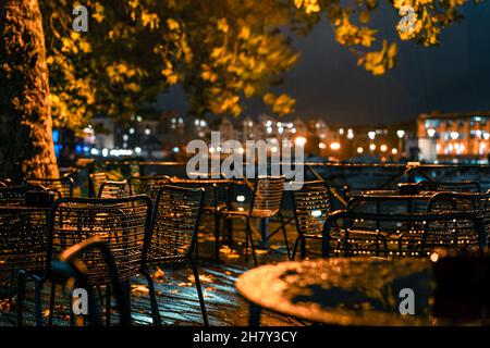 City cafe terrazza vicino al fiume nella piovosa serata autunnale alla luce della lanterna. Gocce d'aria su mobili in metallo per esterni. Urban Fall Concept.Selective Foto Stock
