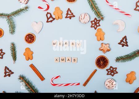 Vista dall'alto corona di Natale fatta di diverse varietà di biscotti di Natale, caramelle, caramelle, arance secche, dolci di pan di zenzero sul dorso blu Foto Stock