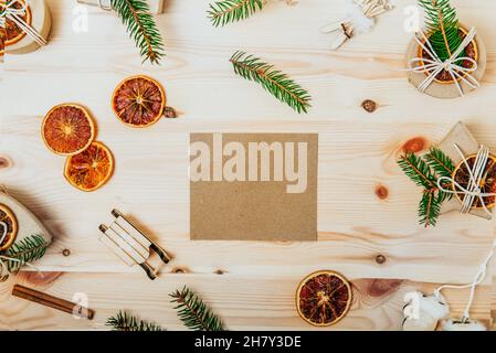 Vista dall'alto cartolina vuota di carta artigianale per saluti e scatole regalo ecocompatibili decorate con abete rosso e arance secche, giocattoli di legno di natale sul de Foto Stock