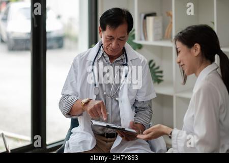 Medico asiatico senior consulenza giovane paziente femminile, parlando con il cliente alla visita di controllo medico. Trattamento di malattie geriatriche. Anziani Foto Stock