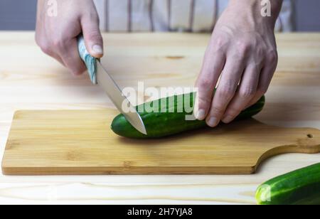 Un giovane taglia con cura un cetriolo con un coltello su un tagliere Foto Stock