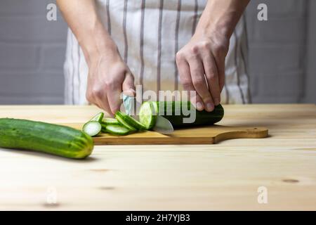 Un giovane taglia con cura un cetriolo con un coltello su un tagliere Foto Stock