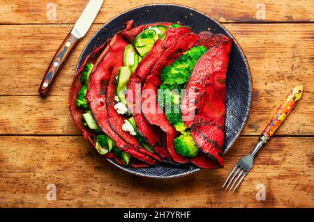 Piatto di frittelle di barbabietole farcite con verdure su tavola rustica in legno Foto Stock